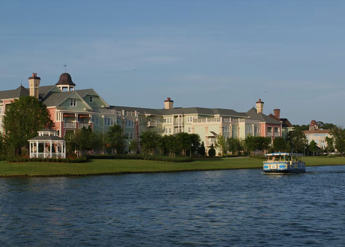 Disney World lakeside pastel resort with gazebo and sightseeing boat on calm water under blue sky Disney World lakeside pastel resort with gazebo and sightseeing boat on calm water under blue sky
