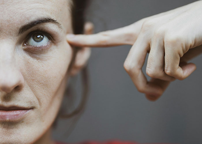 Close-up of a woman pointing to her head, illustrating habits and behaviors associated with neurodivergent people.