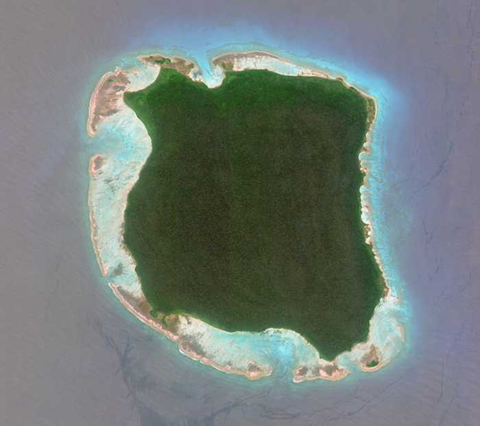 Aerial view of a remote forbidden place on Earth, showing dense green vegetation surrounded by shallow turquoise waters.