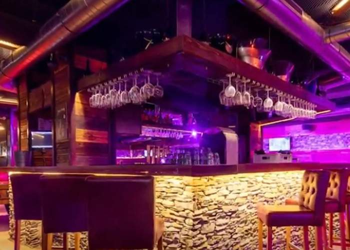 Interior of Swiss bar with stone wall counter and hanging glasses, related to waitress who escaped Swiss bar fire claims.