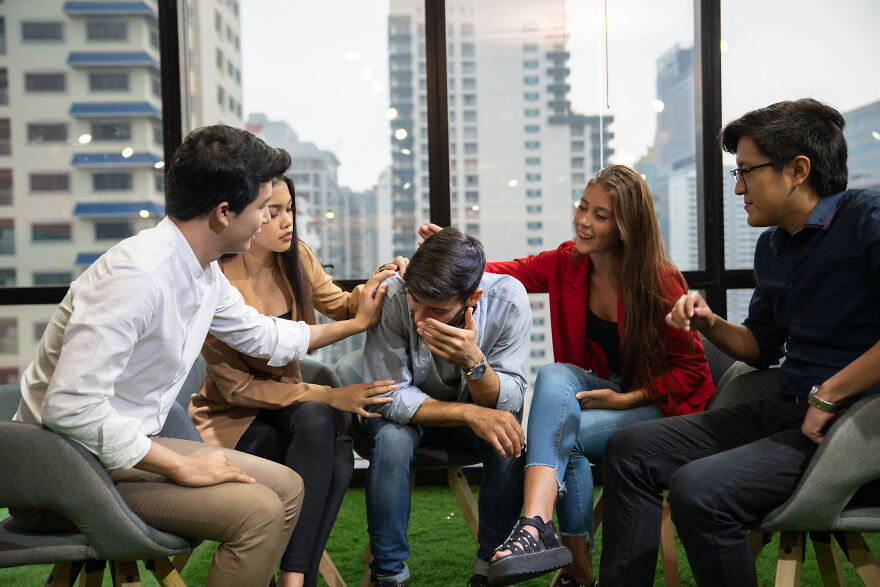 Group of friends gathered indoors, encouraging a man opening up and sharing secrets during paranoia questions game.
