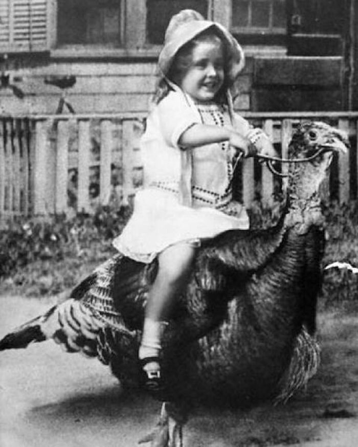 Black and white photo of a young girl riding a giant turkey in an odd and creepy vintage setting.