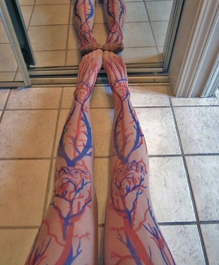 Legs with detailed red and blue body art illustrating veins and arteries, reflected on a tiled floor near a mirror, medical pics.