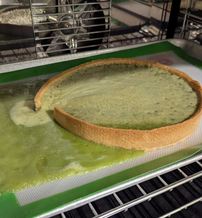 Partially baked dessert crust leaking filling onto baking sheet inside an oven, showing ways people managed to ruin dessert.