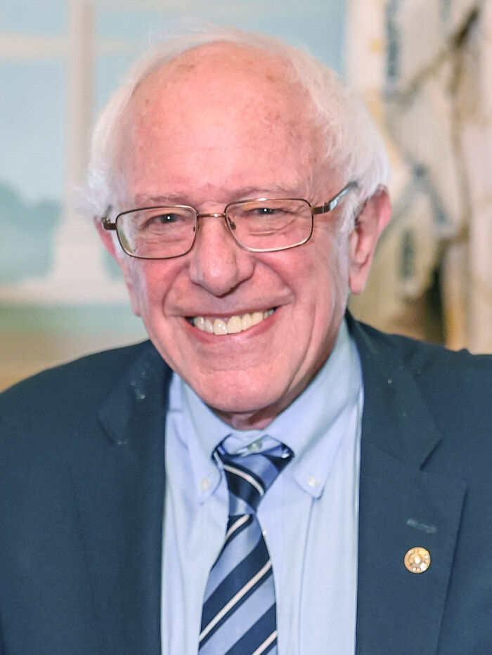 Older man in glasses smiling in a suit and striped tie, indoor portrait, rained frogs