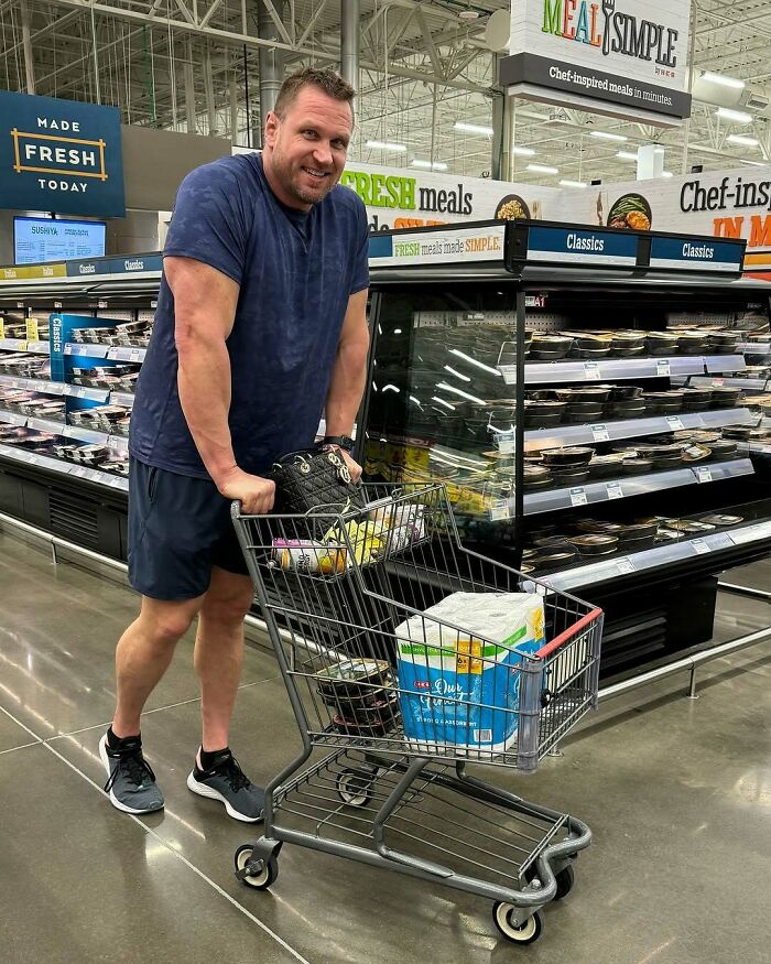 Tall man shopping in a grocery store, pushing a small cart that highlights struggles only tall people face.