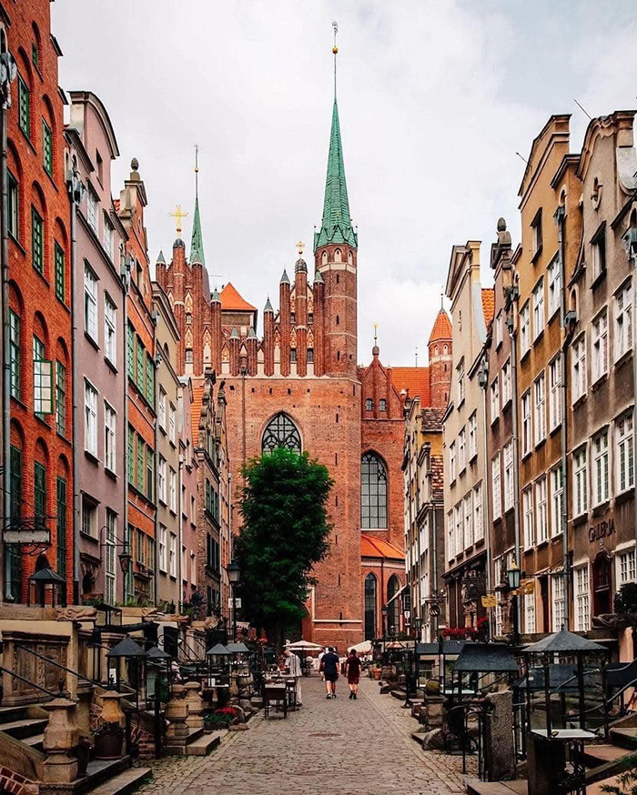Historic European street with Gothic church tower in the background, representing countries that sleep the most according to OECD data.