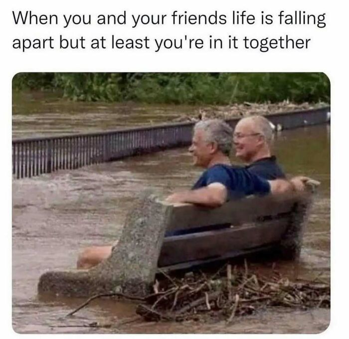 Two men sitting on a bench in floodwater, smiling, illustrating relatable memes about life as an introvert and friendship.