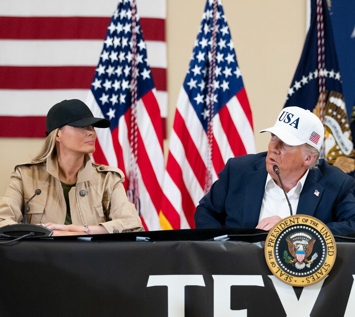 Melania Trump and Donald Trump at Mar-a-Lago event with USA hats and American flags in the background, showing body language. Melania Trump and Donald Trump at Mar-a-Lago event with USA hats and American flags in the background, showing body language.