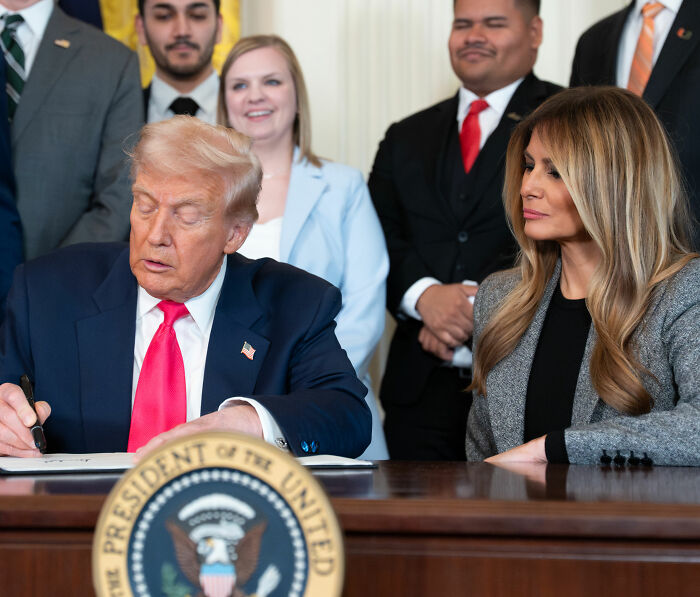Melania Trump's body language observed closely as Donald Trump signs documents with onlookers behind them. Melania Trump's body language observed closely as Donald Trump signs documents with onlookers behind them.