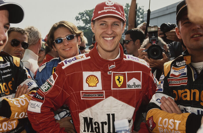 Race car driver in red Ferrari suit smiling among drivers and photographers, highlighting celebrities who didn’t deserve downfall.