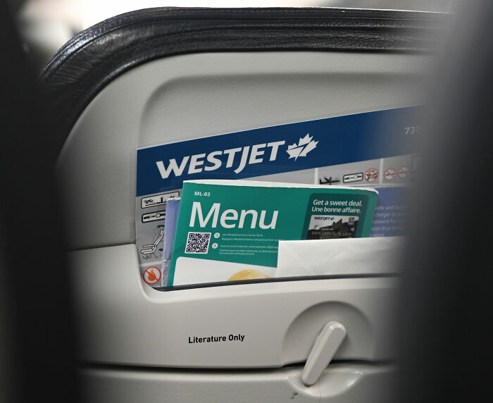 Sardine can seating close-up of WestJet seat pocket with menu in cramped airplane cabin Sardine can seating close-up of WestJet seat pocket with menu in cramped airplane cabin