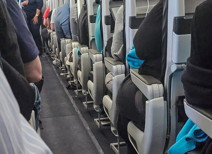 Cramped airplane cabin showing sardine can seating with narrow aisle and passengers squeezed into tight legroom. Cramped airplane cabin showing sardine can seating with narrow aisle and passengers squeezed into tight legroom.