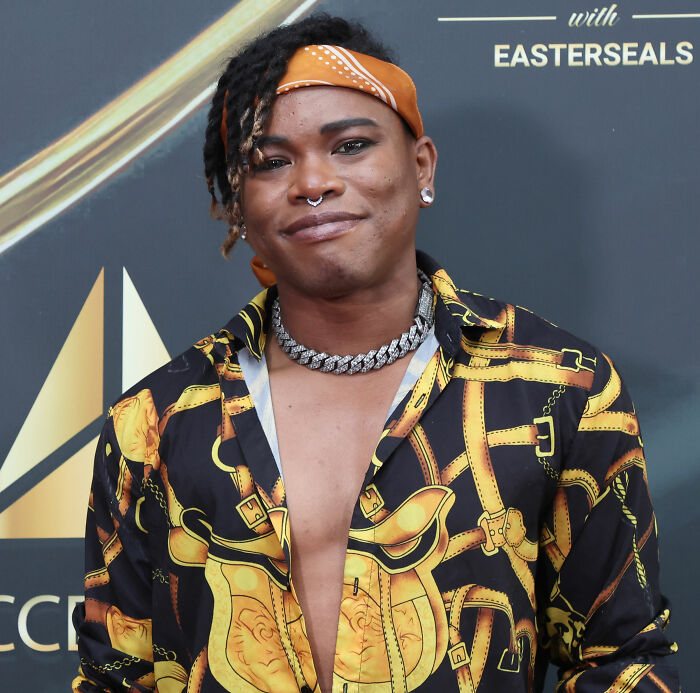 Person wearing an open patterned shirt and orange headband at an event related to Will Smith accused of harassing musician. Person wearing an open patterned shirt and orange headband at an event related to Will Smith accused of harassing musician.