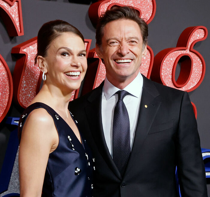 Hugh Jackman and Sutton Foster smiling together at an event highlighting fans spotting six fingers in beach photos.