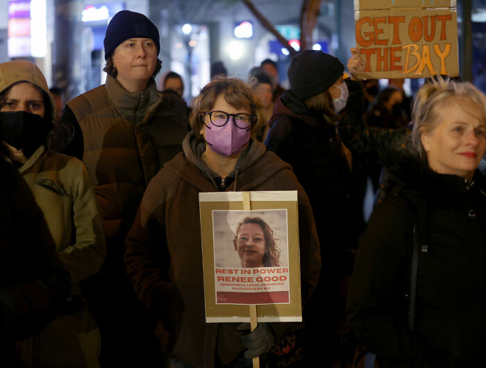 Protesters gathered at night, one holding a sign honoring slain mom Renee Good during ICE agent incident demonstration. Protesters gathered at night, one holding a sign honoring slain mom Renee Good during ICE agent incident demonstration.