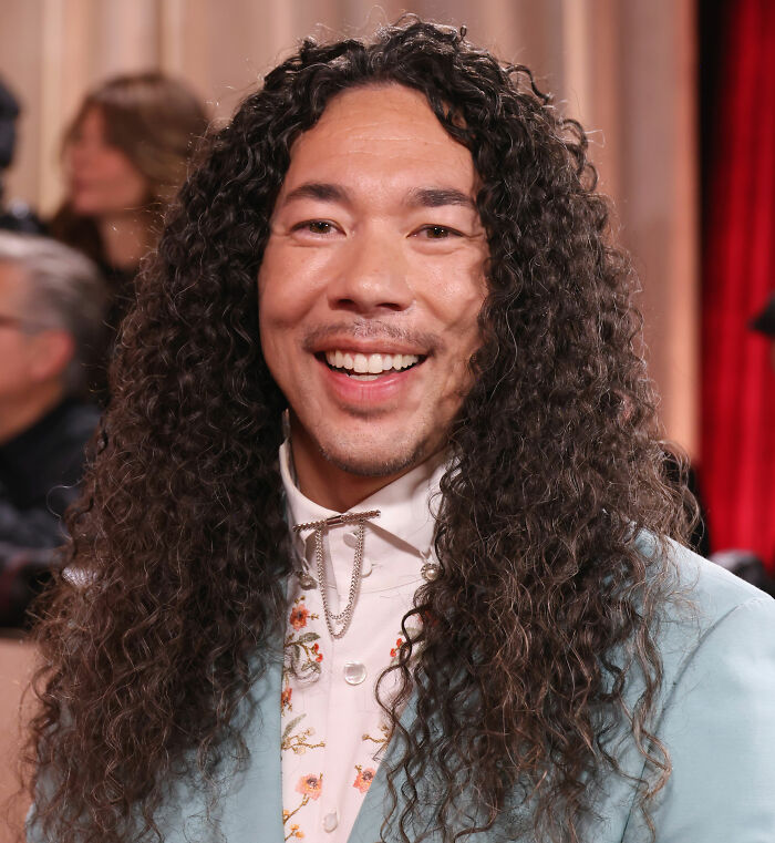 Man with long curly hair smiling at an event highlighting Jennifer Lopez rude interaction backlash at the Golden Globes.