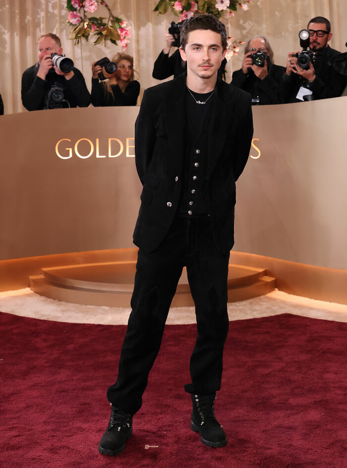 Timothée Chalamet on the red carpet at the Golden Globes event, dressed in black with photographers in the background. Timothée Chalamet on the red carpet at the Golden Globes event, dressed in black with photographers in the background.