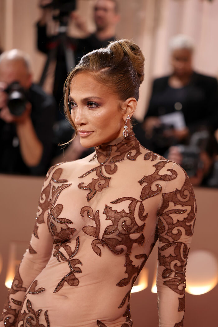 Jennifer Lopez at Golden Globes wearing an intricate sheer gown, sparking ageist backlash over her bold fashion choice.