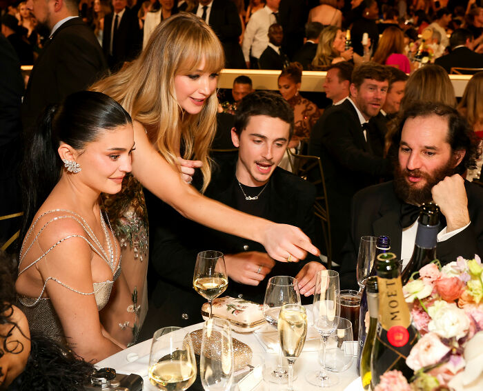 Celebrities enjoying Golden Globes food at a formal event, with drinks and elegant table settings visible.