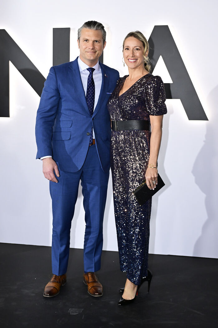 Man in blue suit and woman in sparkly black dress posing together at a MAGA documentary premiere event.