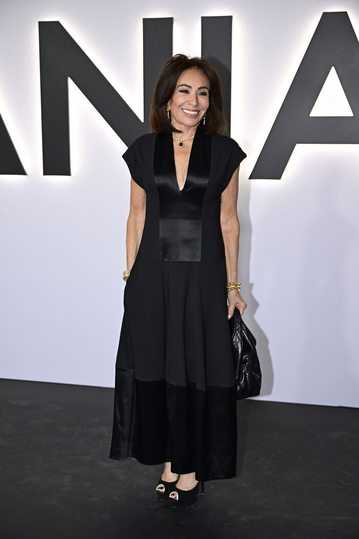 Woman in a black dress and gold jewelry posing at an event with large letters in the background, highlighting MAGA looks.