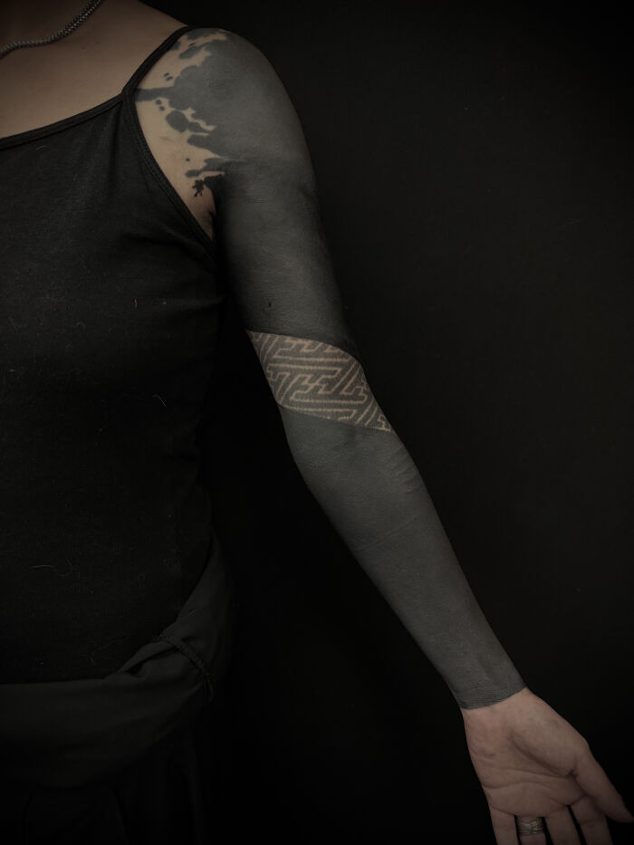 Blackout and geometric patterns tattoo sleeve on arm, showcasing cool tattoos that almost don’t feel real against dark background.