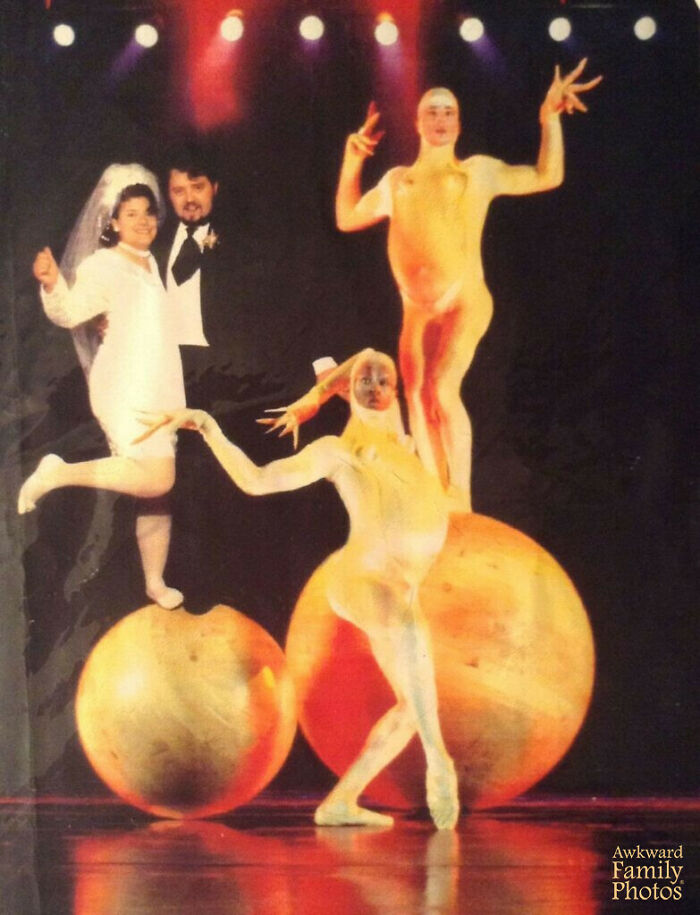 Bride and groom posing awkwardly on large balls with two performers in yellow body suits on stage, awkward wedding photos.