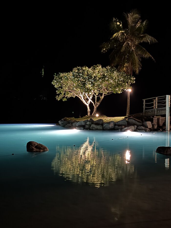 Turquoise shade of blue water glowing at night near a small island with palm trees in French Polynesia.