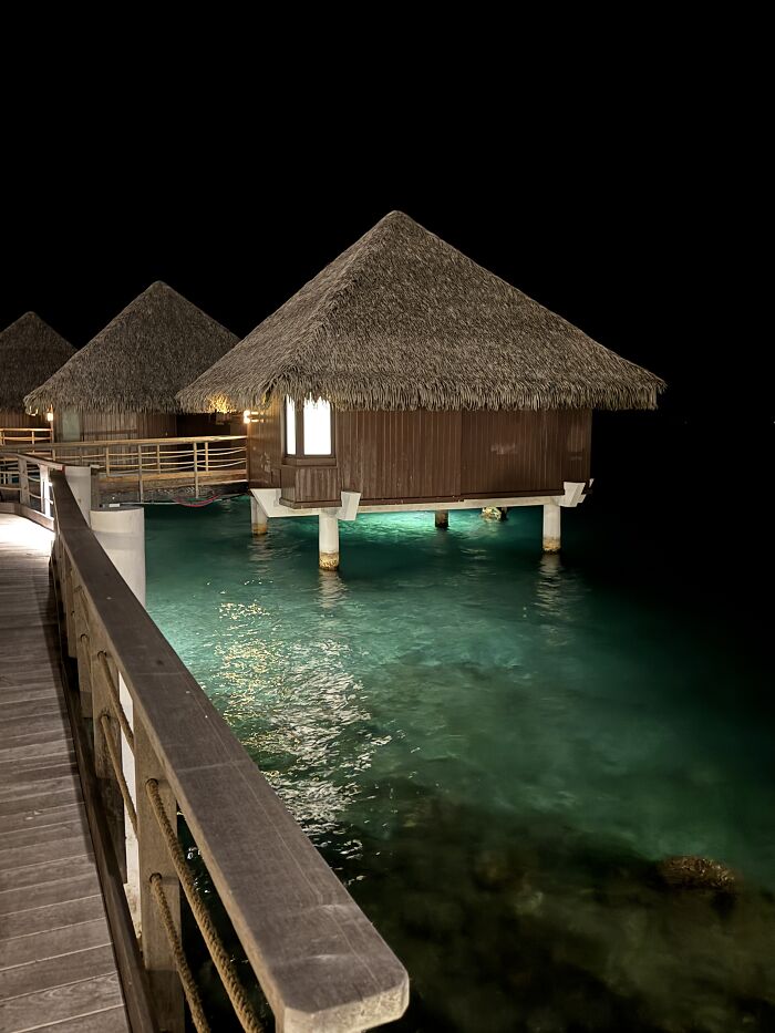 Overwater bungalows glowing above clear turquoise waters at night in French Polynesia with vibrant blue shades.
