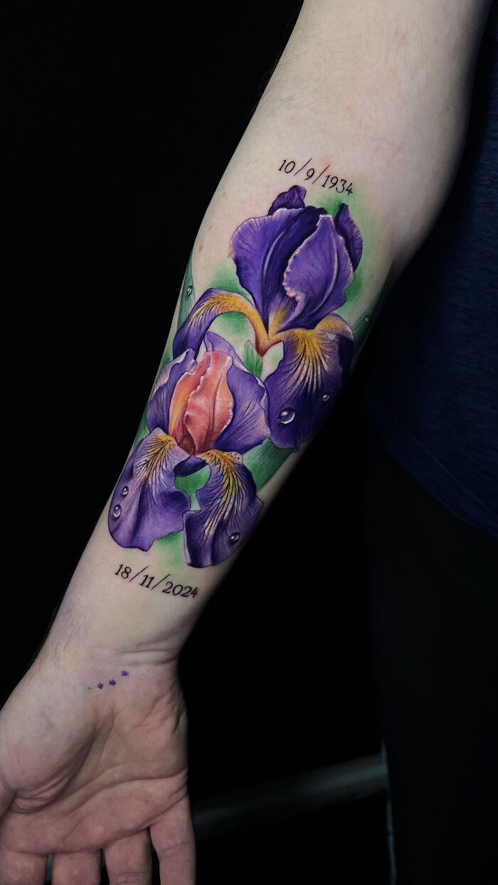 Vibrant purple iris flower tattoo on forearm with realistic water droplets and dates, showcasing cool tattoos artistry.