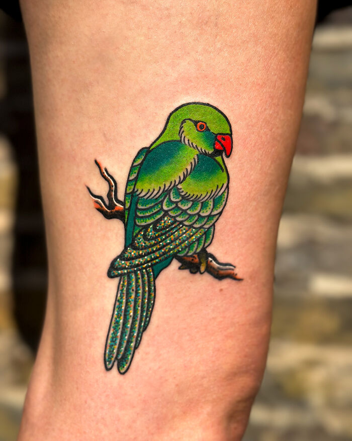 Bright green parrot tattoo on skin with detailed feathers, branch, and vibrant colors, showcasing cool tattoos that look almost unreal.