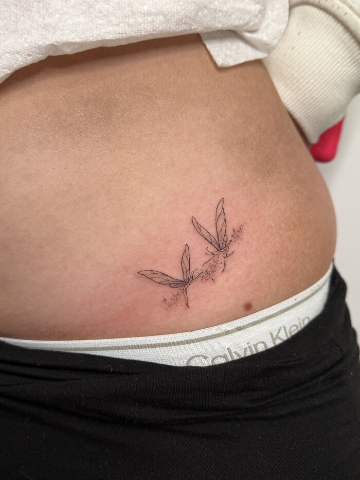 Minimalist fine line tattoo of two delicate dragonflies on the lower abdomen, showcasing cool tattoos that look almost unreal.