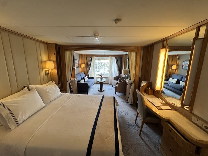 Luxurious cruise cabin with a king bed, seating area, and window view of blue waters in French Polynesia.