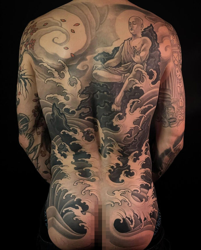 Intricate back tattoo featuring a meditating figure and dynamic waves, showcasing cool tattoos that look almost unreal.