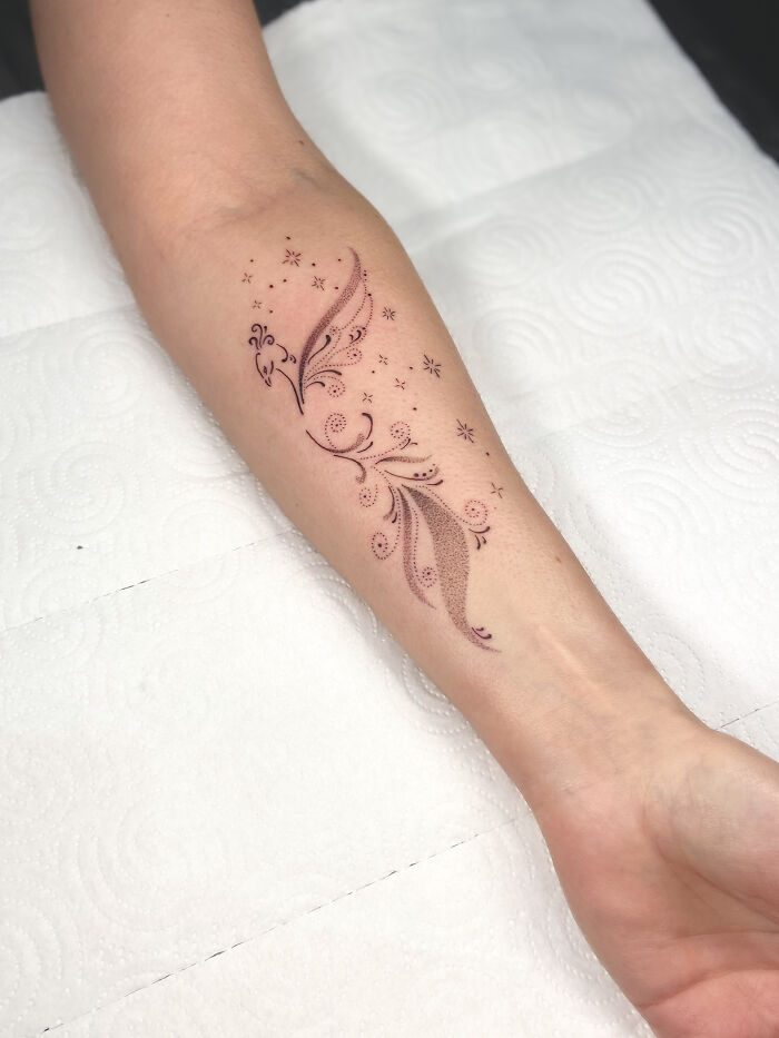 Delicate phoenix tattoo on forearm with fine dot work and star accents, showcasing cool tattoos that look almost unreal.