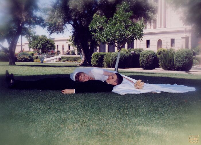 Bride and groom lying awkwardly on grass in a wedding photo capturing a memorable awkward wedding moment outside a building.