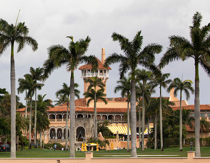Mar-a-Lago estate with tall palm trees, hosting a creepy event with people in dog masks and old-time costumes.
