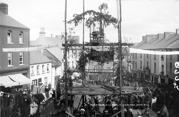 Black and white photo of a large crowd gathered for a strange traditional event with wooden structures and decorations.