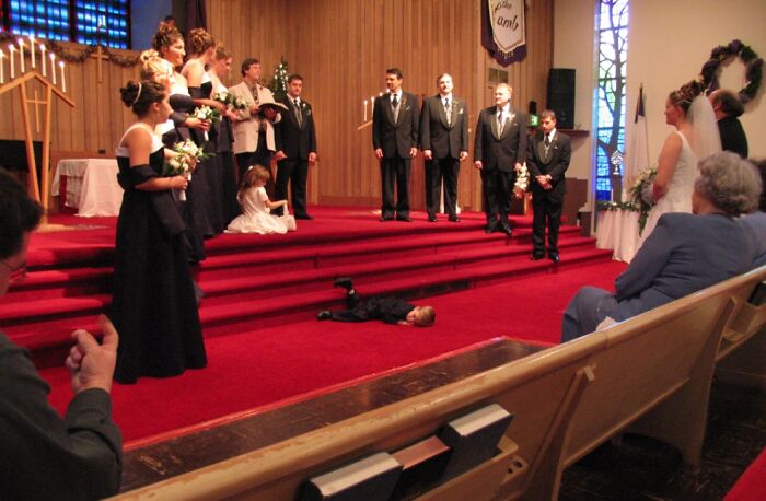 Young boy lying on the floor during a formal wedding ceremony, creating an awkward wedding photo moment.