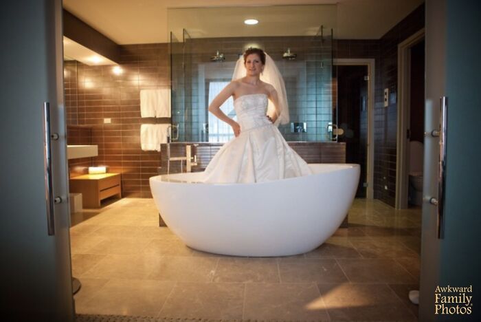Bride in full wedding dress standing inside a bathtub in a modern bathroom in an awkward wedding photo.