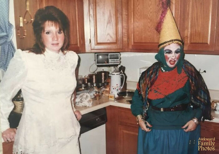 Bride in a vintage wedding dress standing next to a person in a colorful costume in a kitchen, awkward wedding photo moment