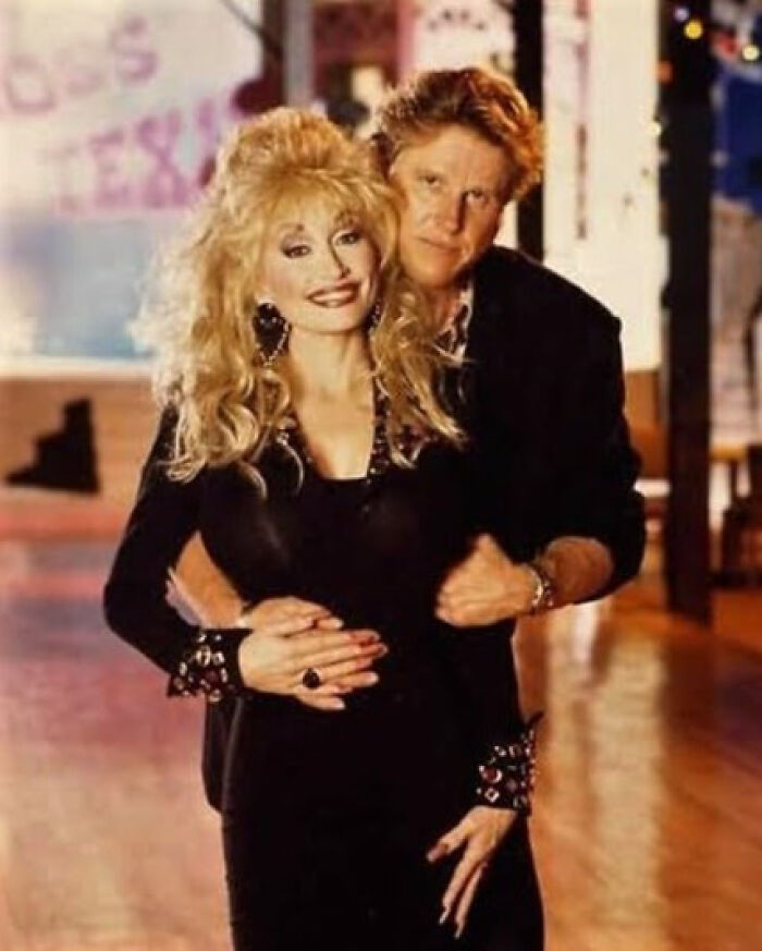 Couple hugging on a dance floor, woman with big blonde hair in a black dress and man behind her, It Rained Frogs