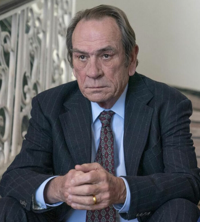 Tommy Lee Jones sitting in a suit with a serious expression as news about daughter Victoria's hotel incident resurfaces.