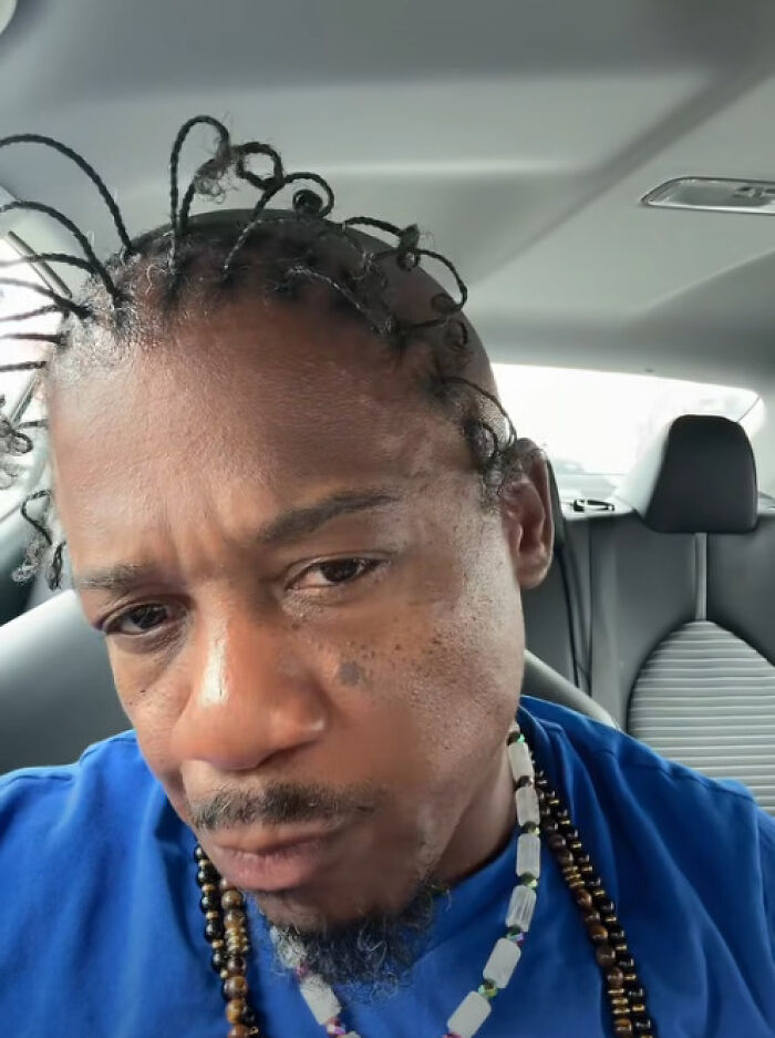 Man with unusual twisted loops hairstyle sitting inside a car, showcasing one of the disastrous hairstyles.