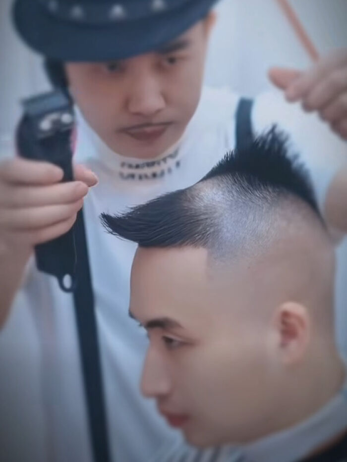 Barber creating a disastrous hairstyle with shaved sides and spiked top on a young man in a salon.