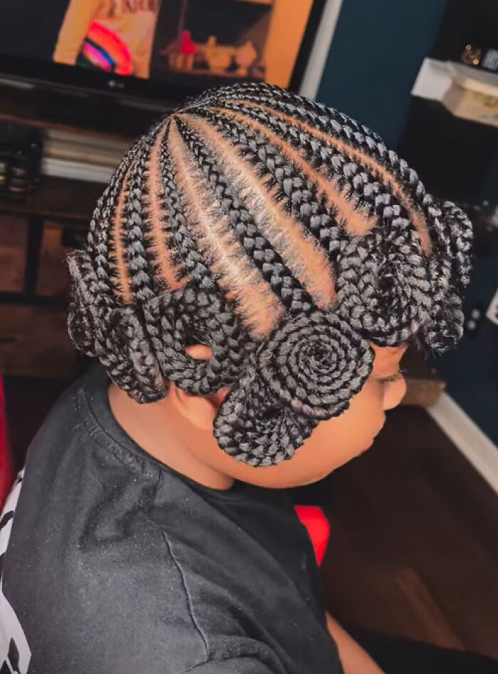 Child with intricate braided hairstyle featuring spiral designs and neat cornrow sections in an indoor setting.