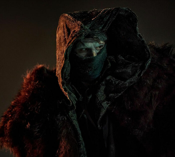 Dark hooded figure with a mask and fur cloak in a dimly lit setting, related to 2026 Oscar nominations coverage.