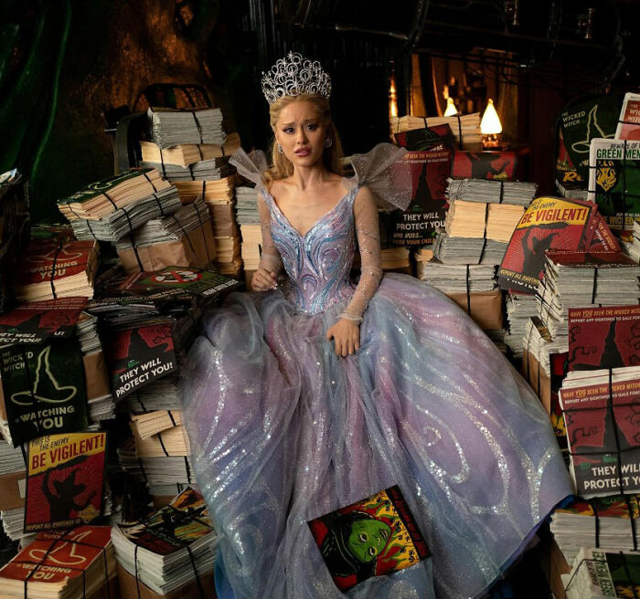 Actress in an elaborate gown and crown surrounded by stacks of books, representing Academy releases 2026 Oscar nominations.