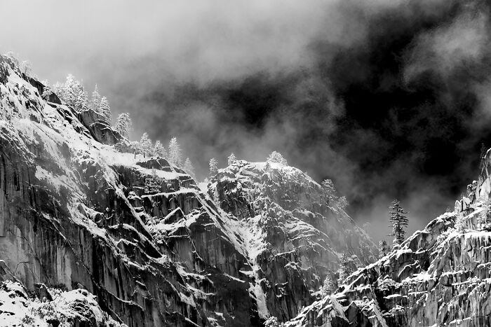 Snow-covered rocky mountain cliffs under a dramatic cloudy sky, showcasing nature's stunning animal photo backdrop.